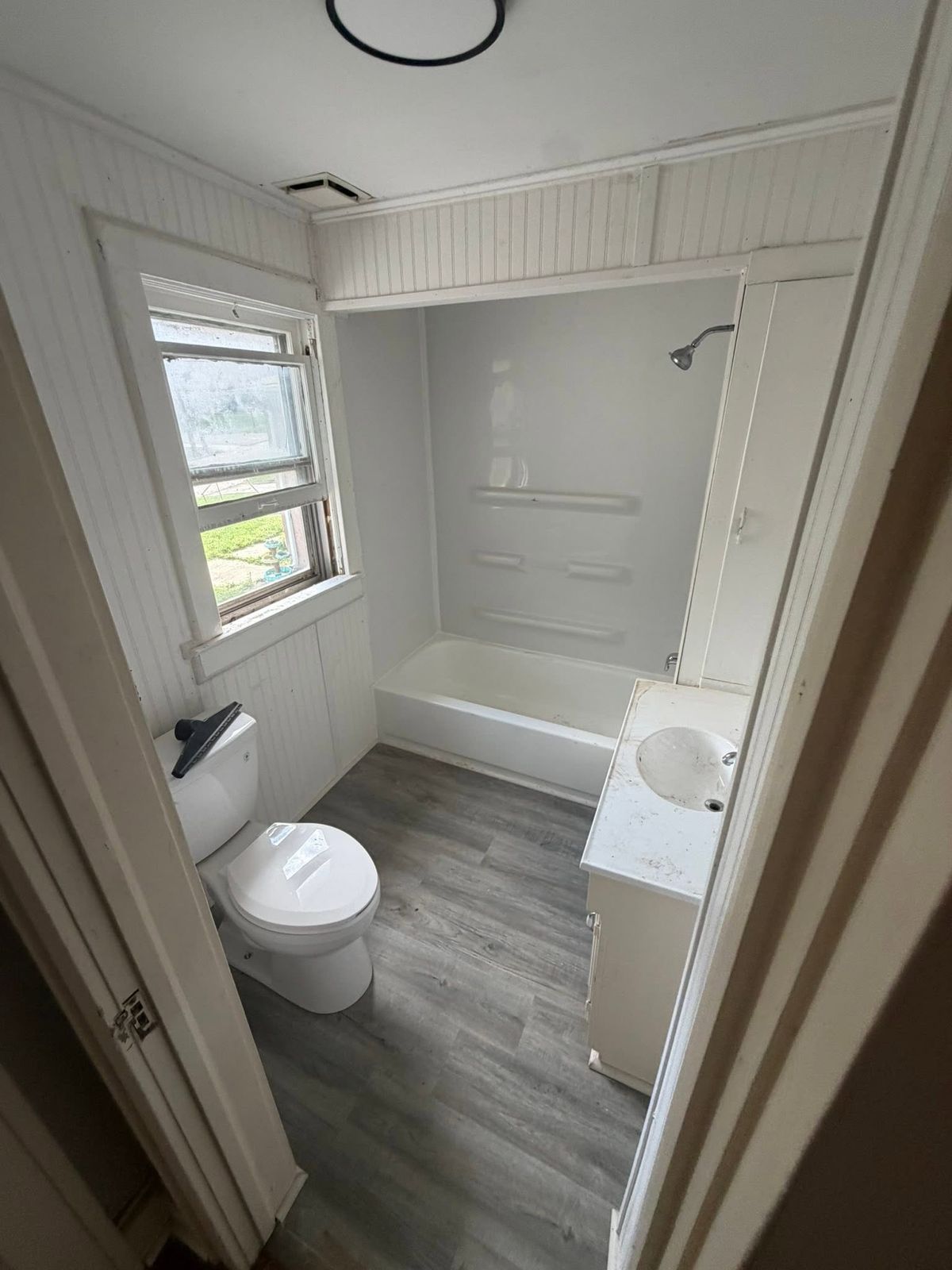 Finished bathroom with white tub and shower surround, vanity and gray vinyl plank floor