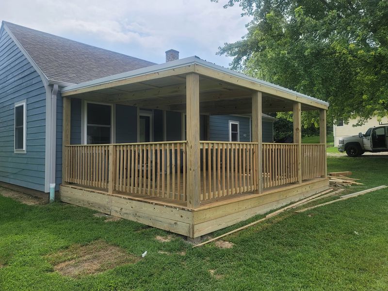 Metal roof over a covered porch added to a blue house, with square wood railings