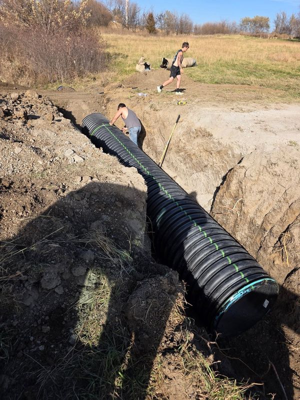 Crew setting a large black corrugated culvert pipe into a trench
