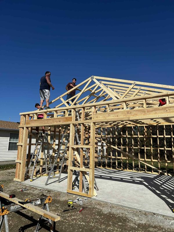 Roof trusses being set on the same framed garage or shop with the crew working up top