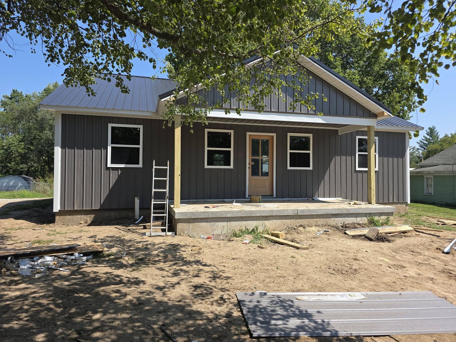 Finished single-story new home with dark vertical siding, a front porch and a fresh dirt yard
