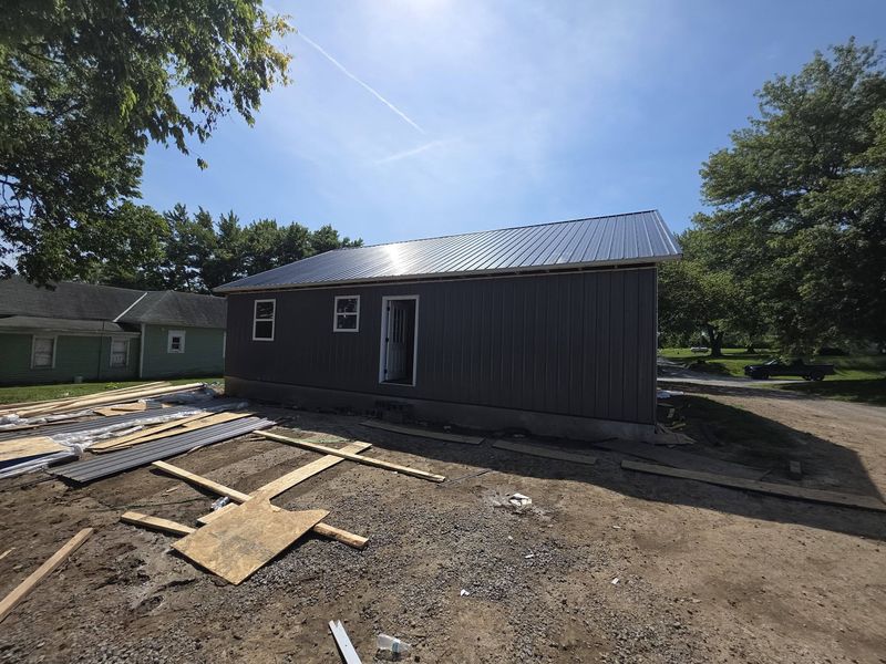 Same home from the side showing the metal roof and a graded dirt lot with lumber staged nearby