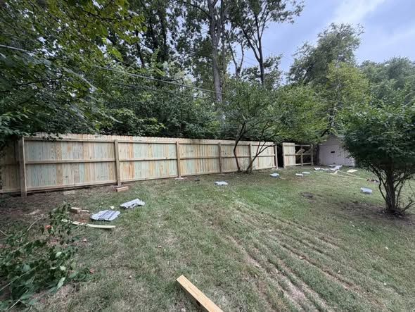 Wood privacy fence built along a tree line at the back of a yard