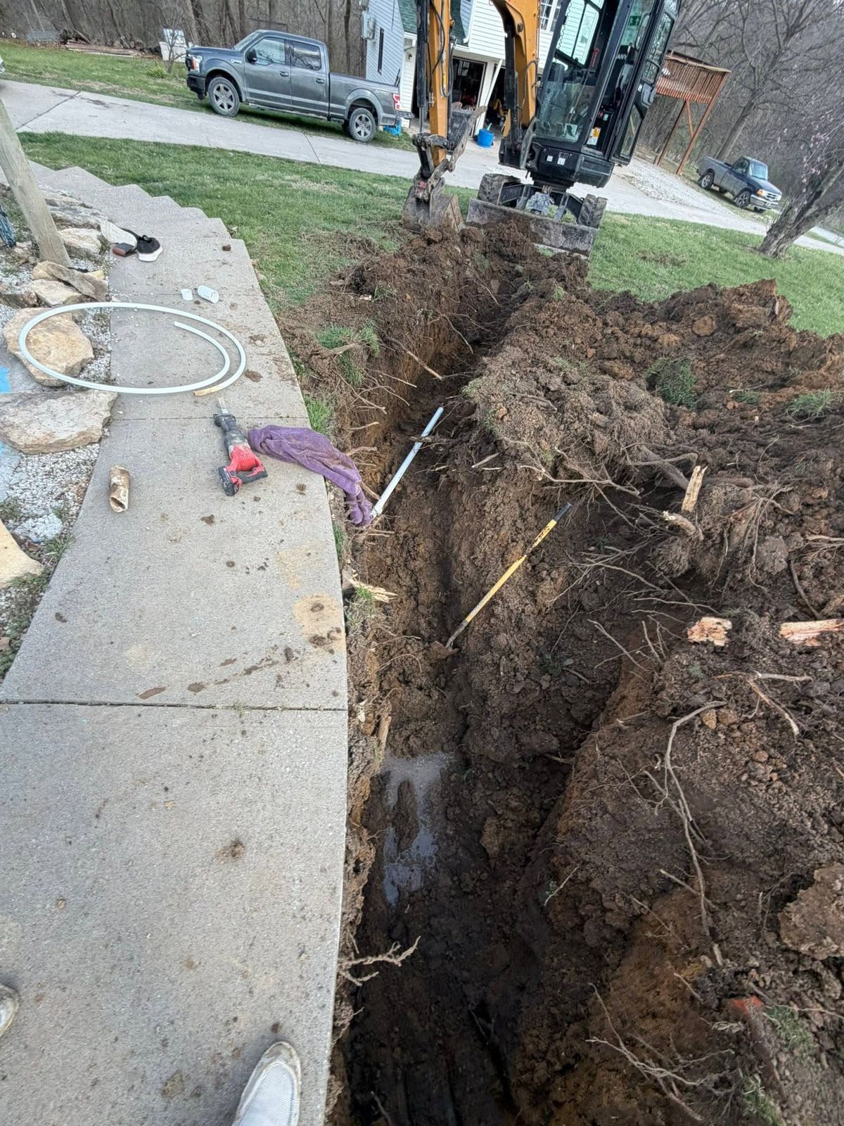 Trench dug along a sidewalk with conduit laid in, excavator bucket above