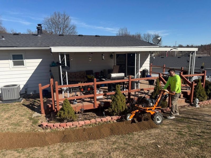 Worker running a walk-behind trencher along a brick-edged landscape bed