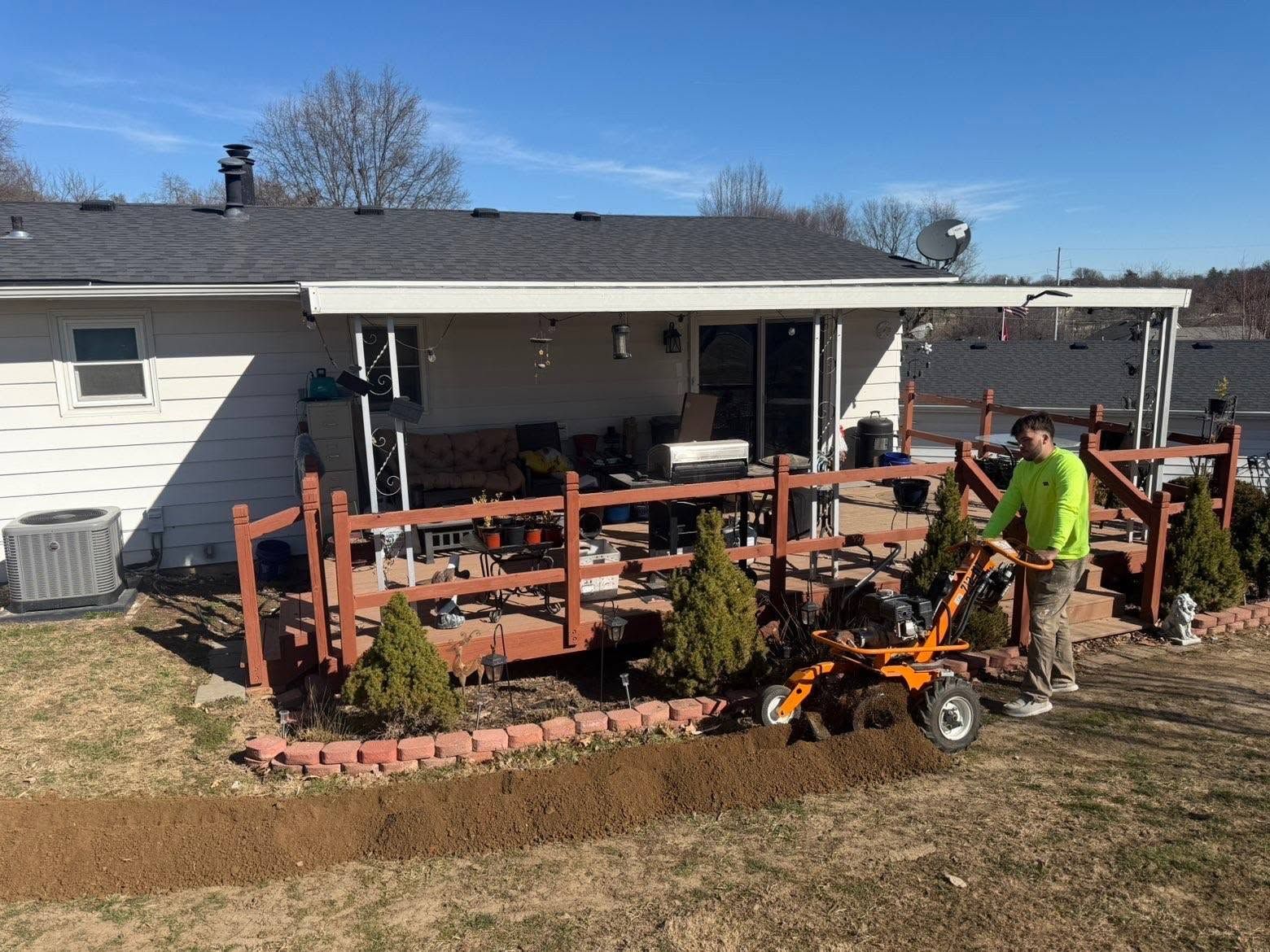 Worker guiding a walk-behind trencher along a brick-edged landscape bed